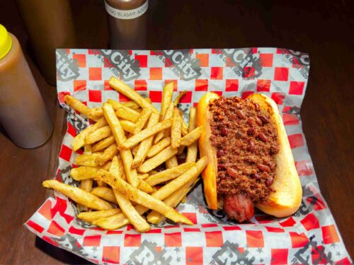 Basket with hot dog and bun covered with chili and side of french fries