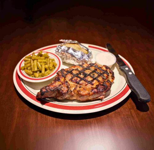 Plate with a grilled smoked porkchop and a side of green beans and baked potato