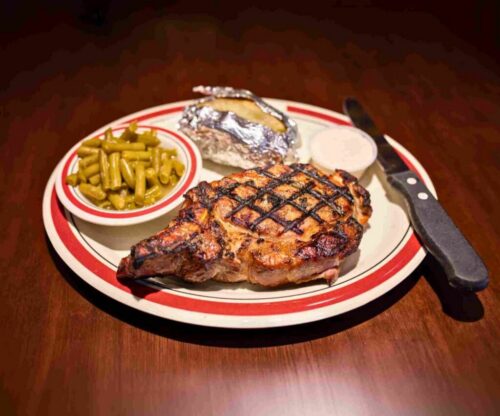 Plate with a grilled smoked porkchop and a side of green beans and baked potato